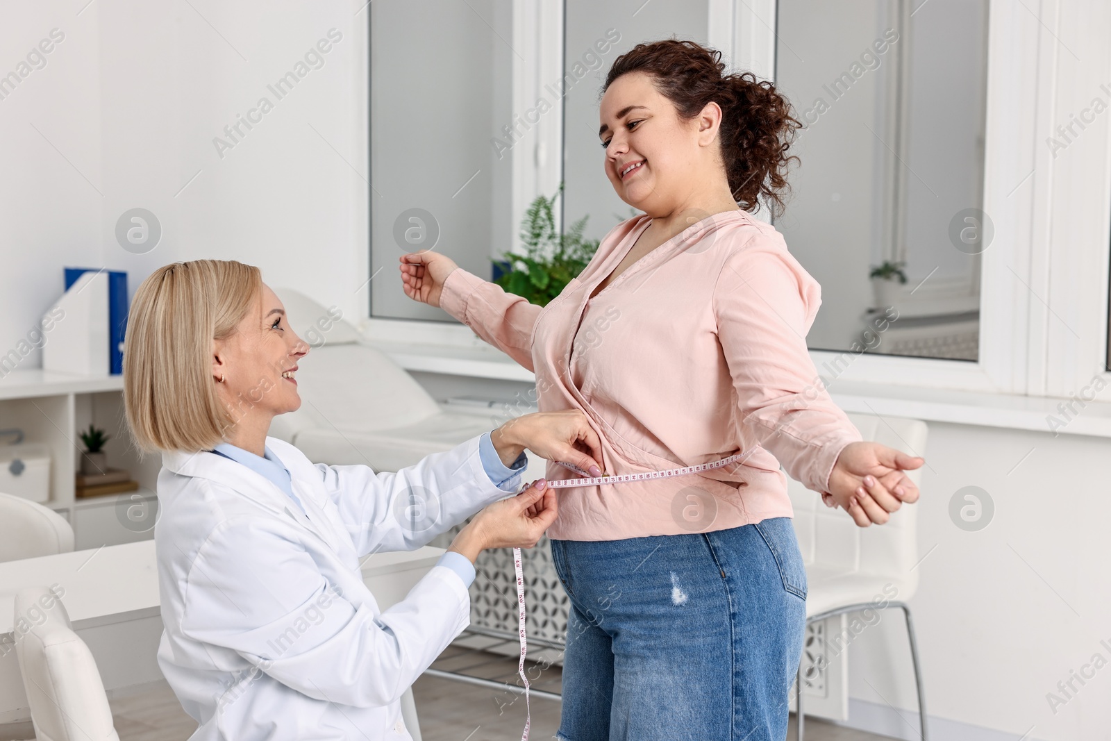 Photo of Happy woman lost weight. Smiling nutritionist measuring patient's waist with tape in clinic