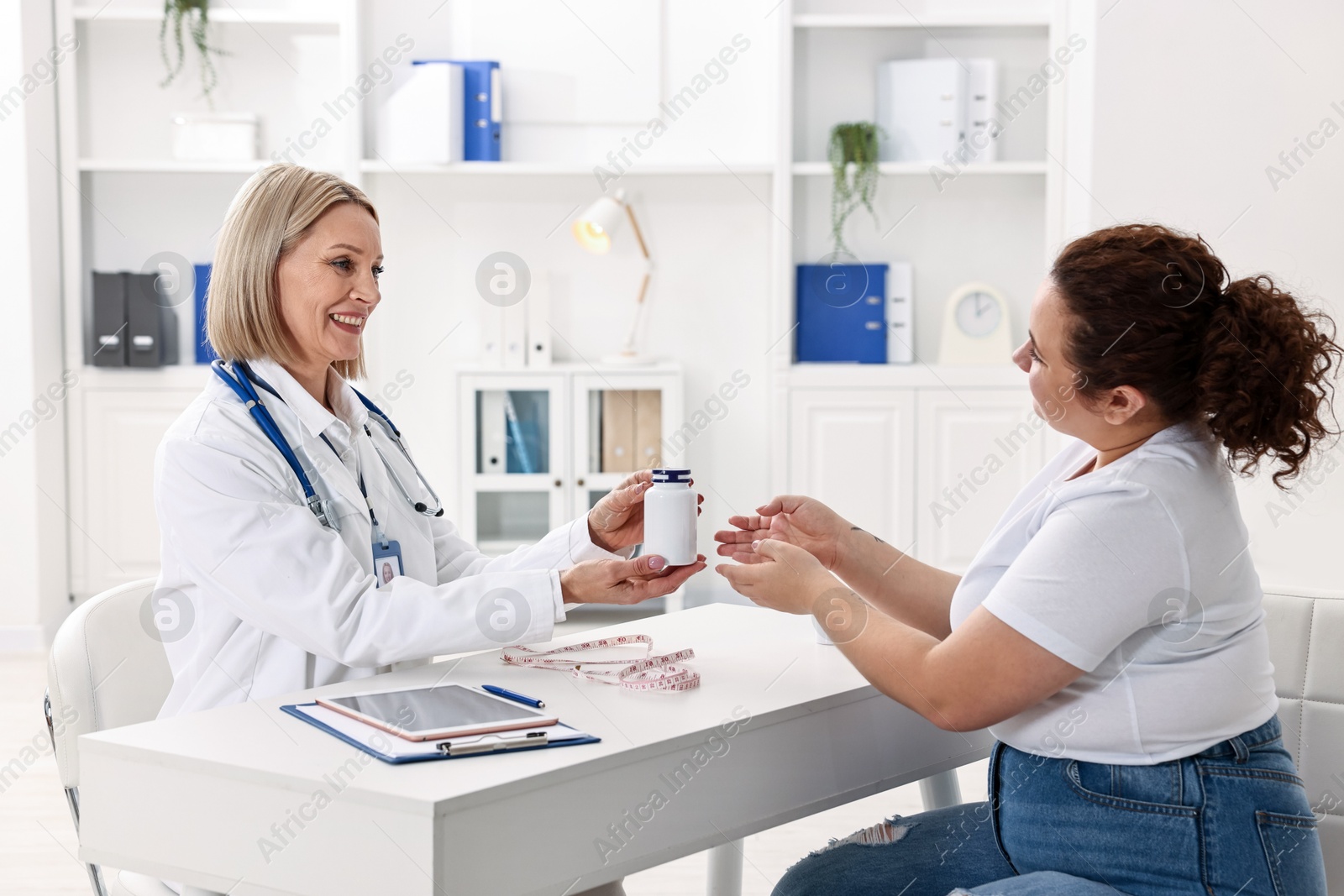 Photo of Weight loss. Smiling nutritionist giving medical bottle with pills to patient at table in clinic