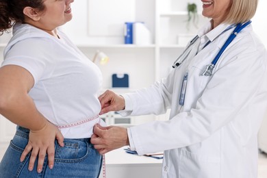 Photo of Weight loss. Smiling nutritionist measuring patient's waist with tape in clinic, closeup