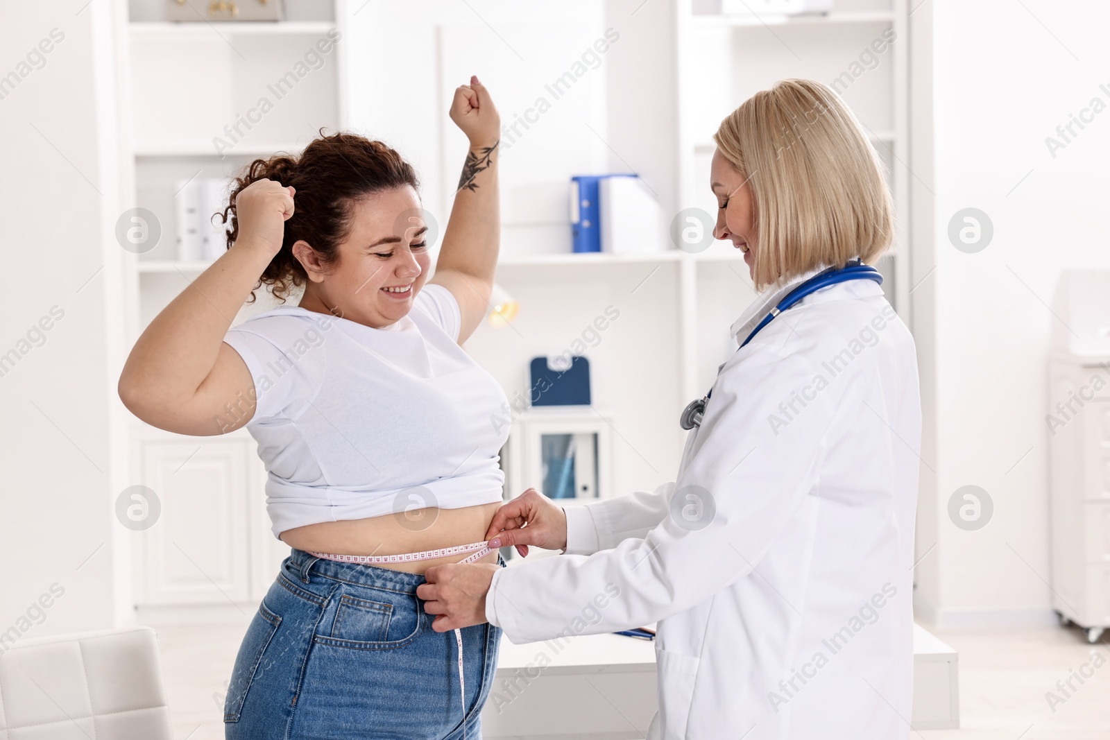 Photo of Happy woman lost weight. Smiling nutritionist measuring patient's waist with tape in clinic