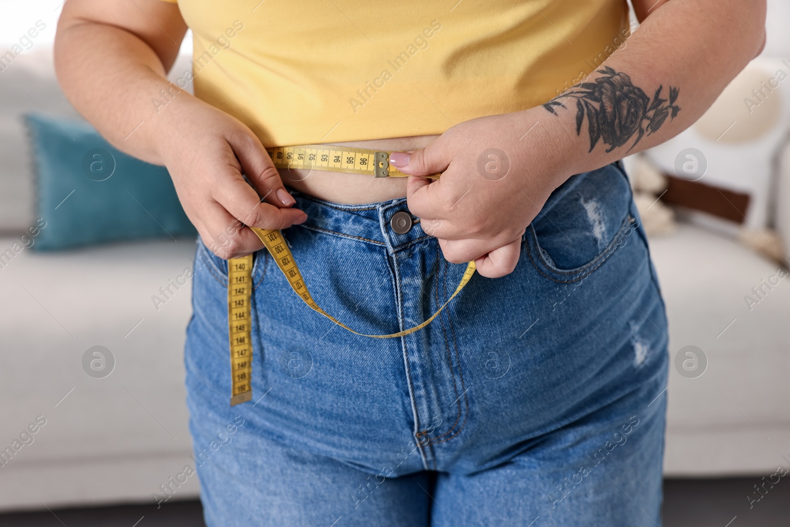 Photo of Weight loss. Plus size woman measuring waist with tape at home, closeup