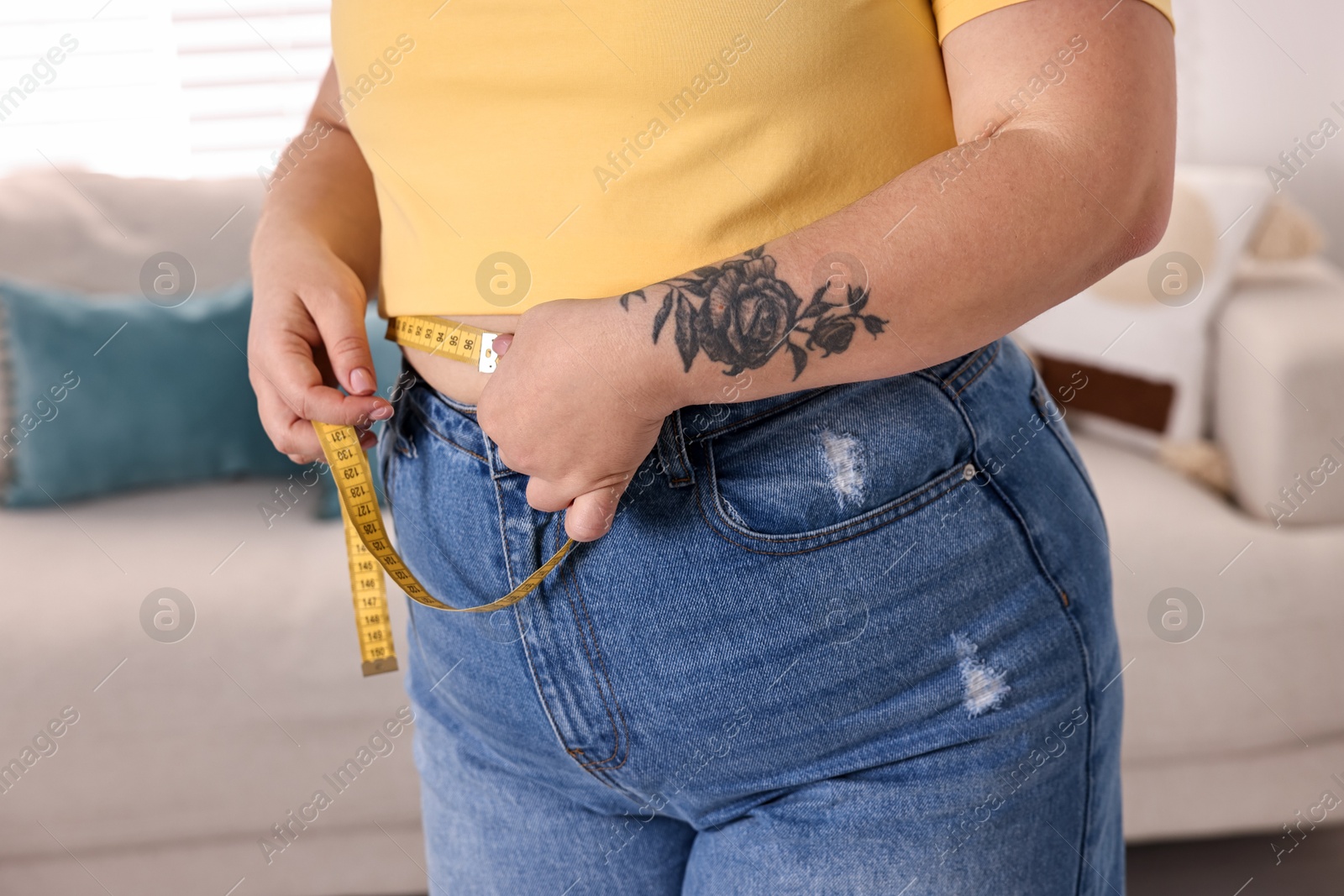 Photo of Weight loss. Plus size woman measuring waist with tape at home, closeup