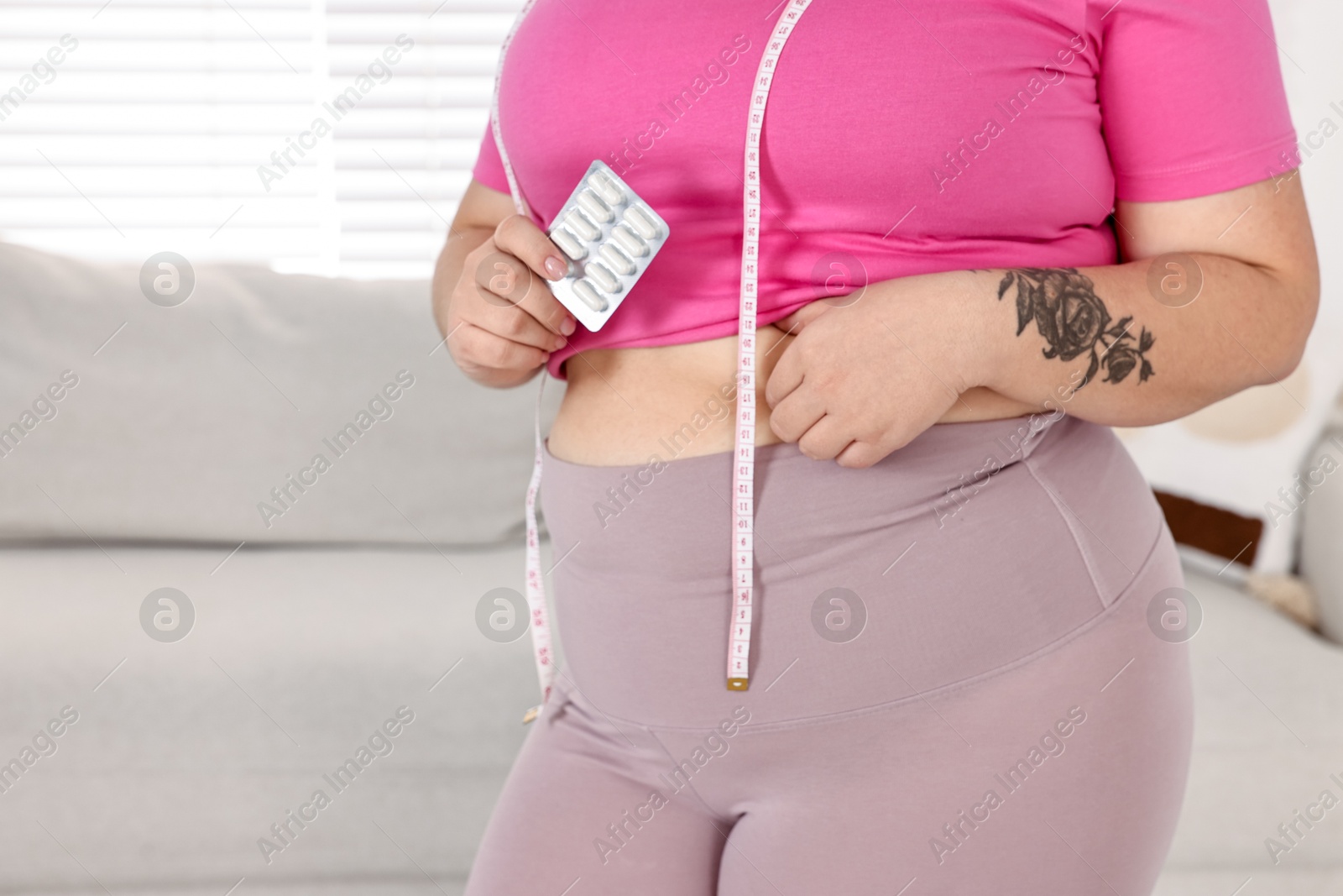 Photo of Plus size woman holding blister of weight loss supplements at home, closeup. Space for text