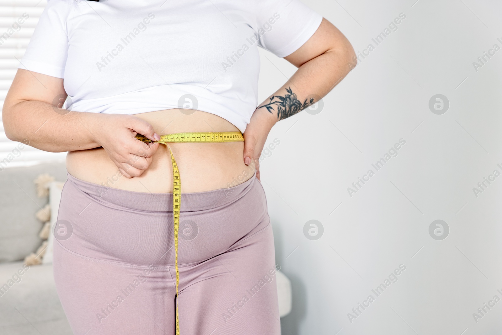 Photo of Weight loss. Plus size woman measuring waist with tape at home, closeup. Space for text