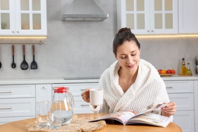 Photo of Beautiful woman with cup of drink reading magazine after spa procedure at wooden table in kitchen