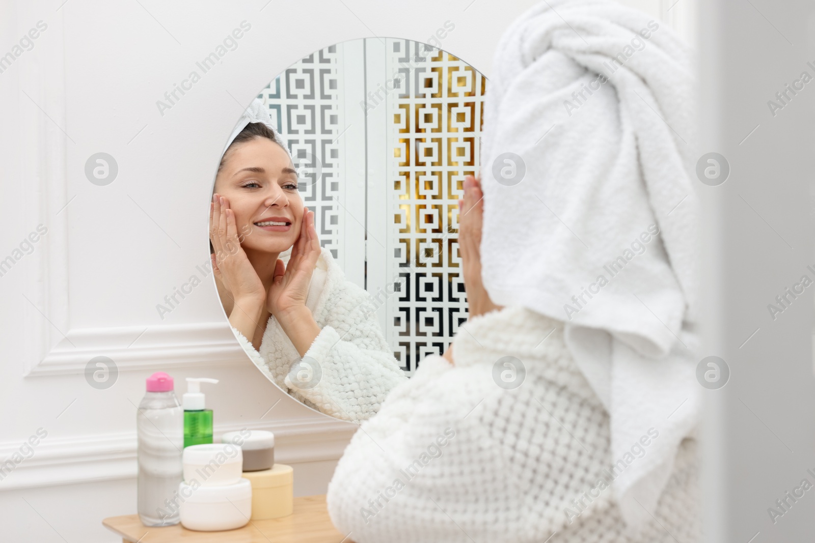 Photo of Spa day. Beautiful woman with towel on head near mirror indoors