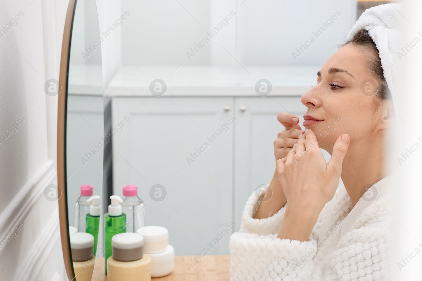 Photo of Spa day. Beautiful woman with towel on head near mirror indoors