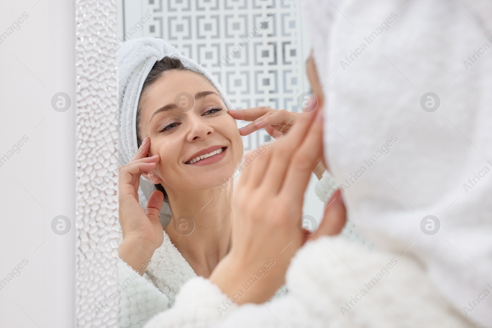 Photo of Spa day. Beautiful woman with towel on head near mirror indoors