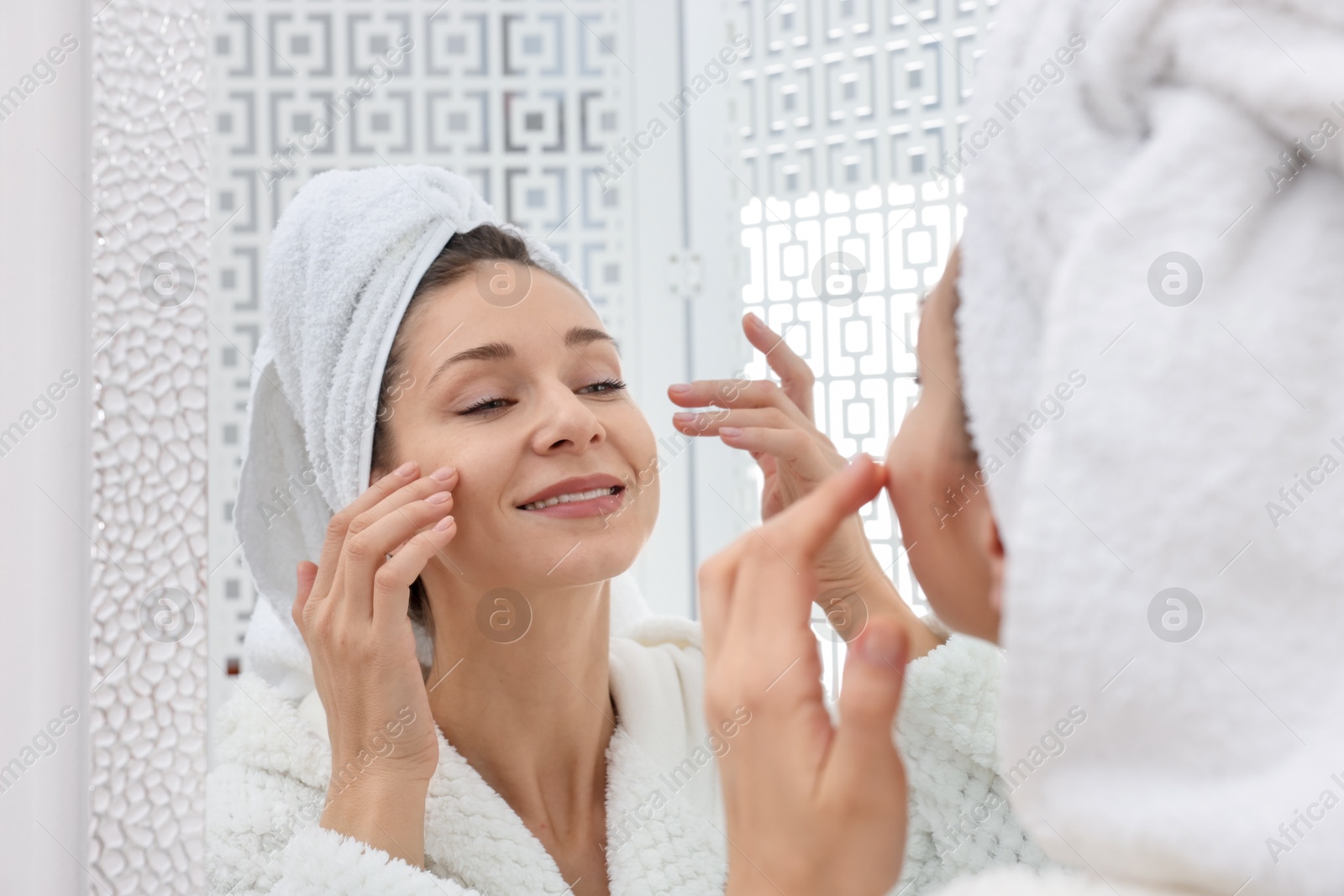 Photo of Spa day. Beautiful woman with towel on head near mirror indoors