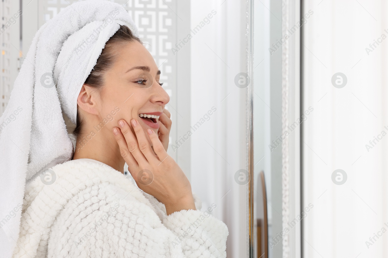 Photo of Spa day. Beautiful woman with towel on head near mirror indoors