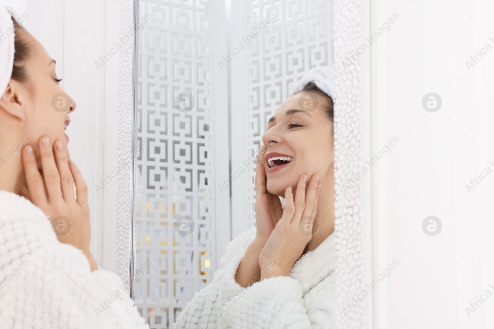 Photo of Spa day. Beautiful woman with towel on head near mirror indoors