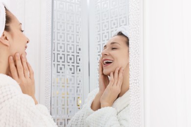 Photo of Spa day. Beautiful woman with towel on head near mirror indoors