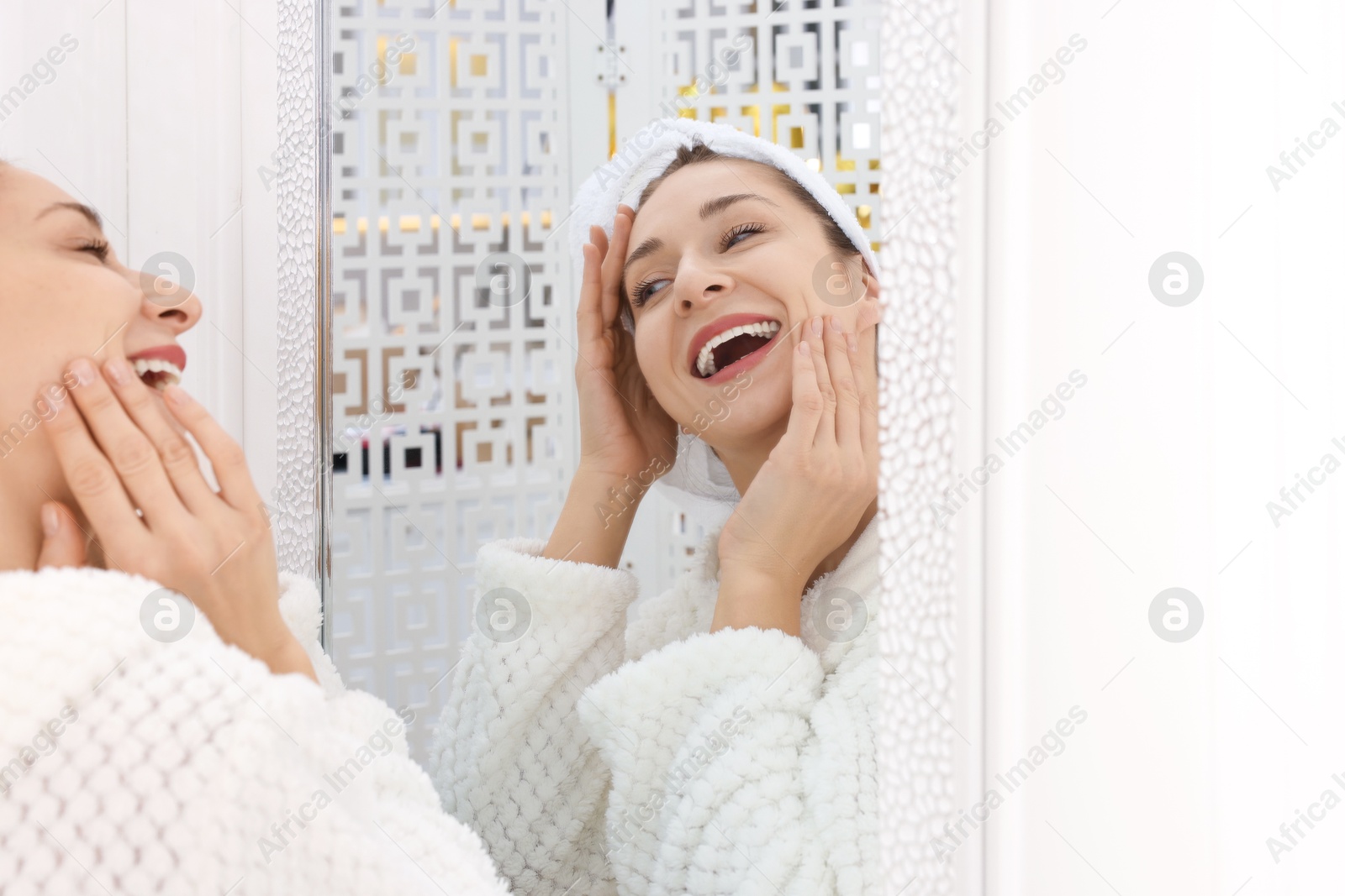 Photo of Spa day. Beautiful woman with towel on head near mirror indoors