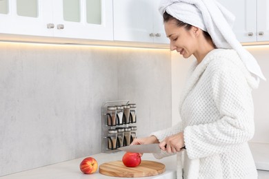 Photo of Beautiful woman cutting apple after spa procedure in kitchen