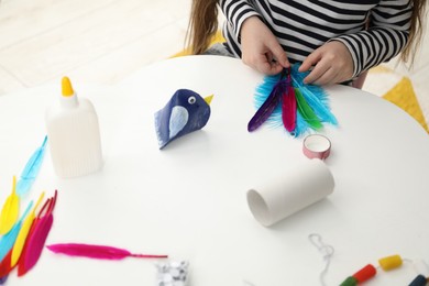 Photo of Little girl making paper bird at white table indoors, closeup. Child handmade craft