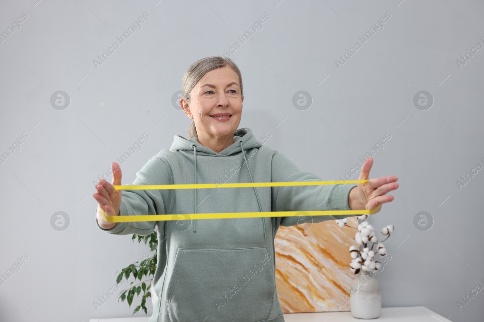 Photo of Smiling elderly woman exercising with fitness elastic band at home