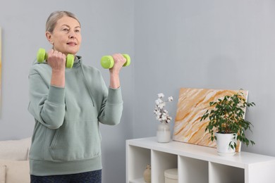 Photo of Elderly woman exercising with dumbbells at home