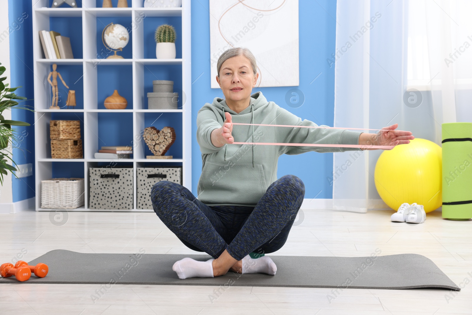 Photo of Elderly woman exercising with fitness elastic band at home