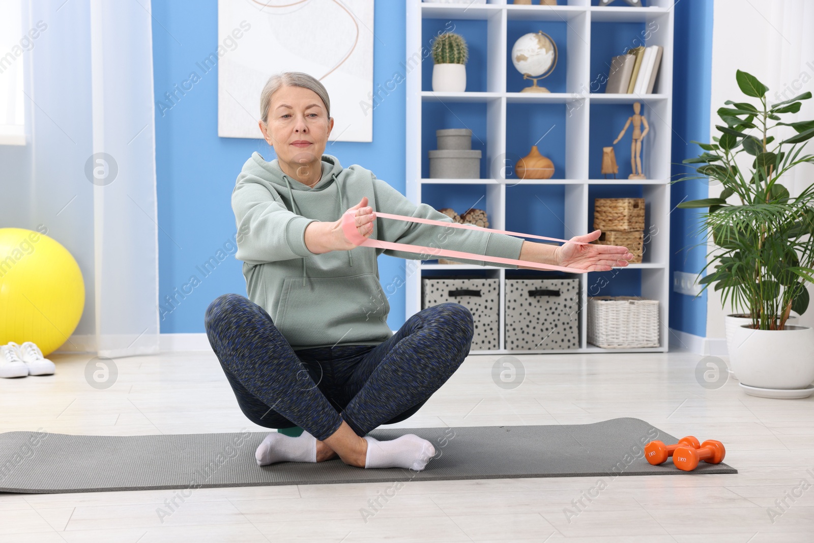 Photo of Elderly woman exercising with fitness elastic band at home