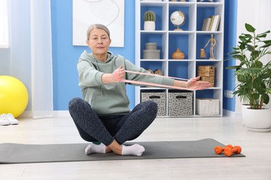 Photo of Elderly woman exercising with fitness elastic band at home