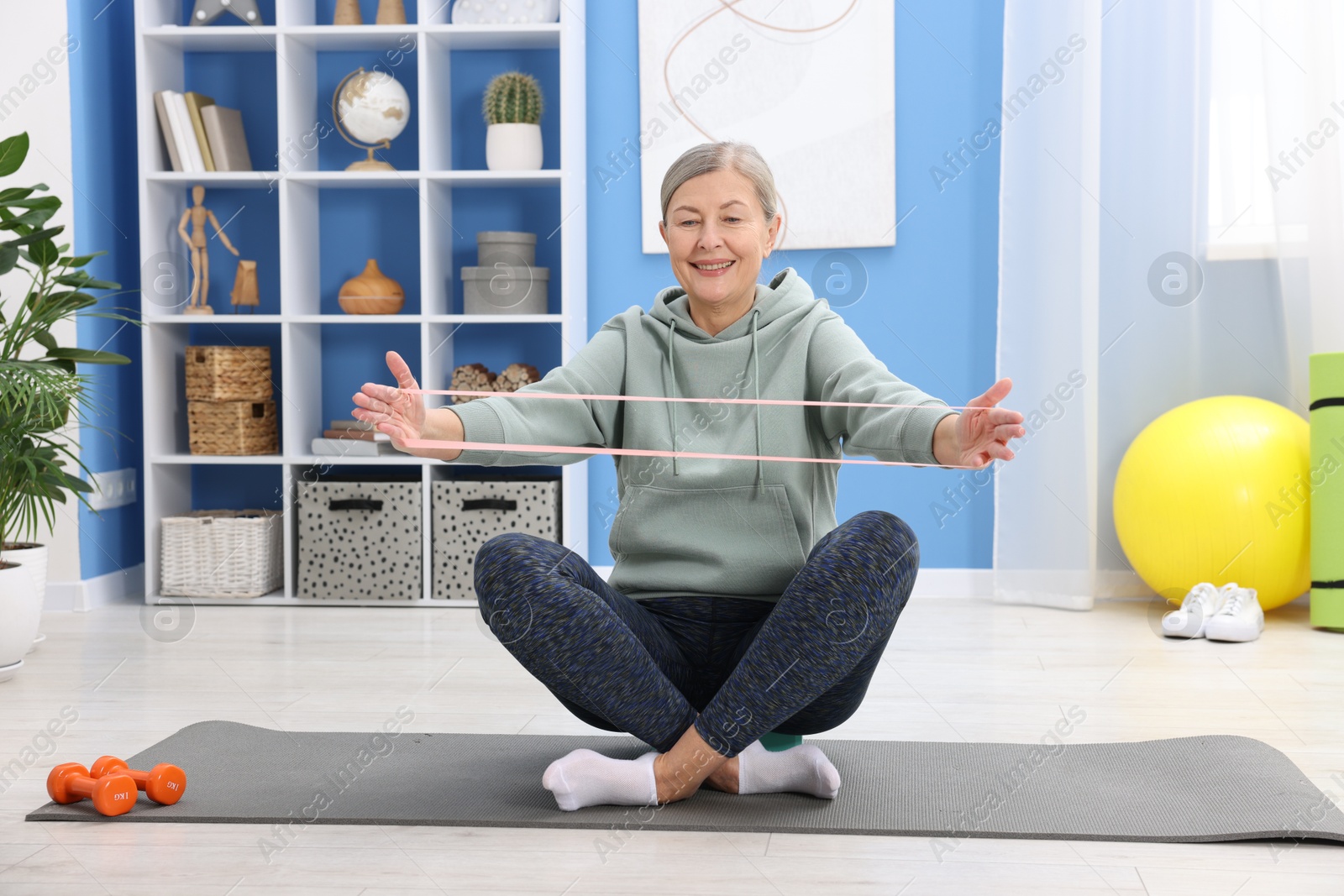 Photo of Smiling elderly woman exercising with fitness elastic band at home