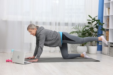 Photo of Elderly woman exercising near laptop at home