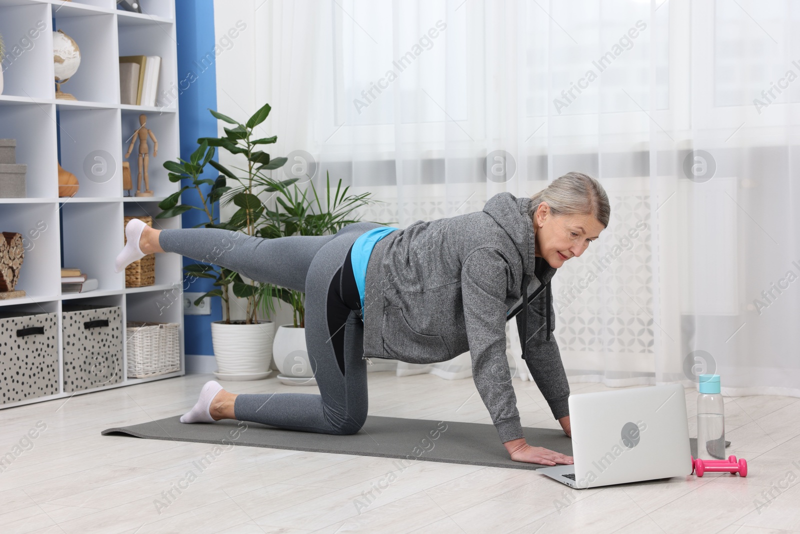 Photo of Elderly woman exercising near laptop at home