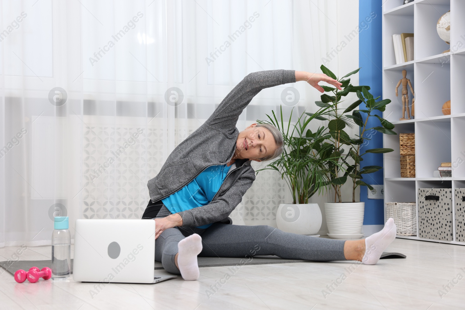 Photo of Smiling elderly woman exercising near laptop at home