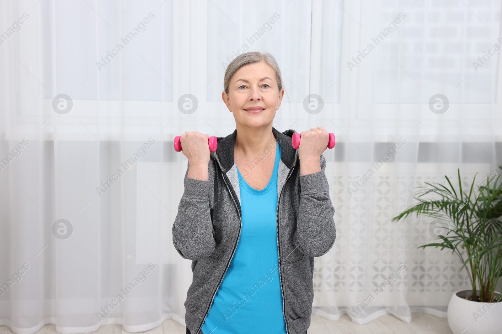 Photo of Smiling elderly woman exercising with dumbbells at home