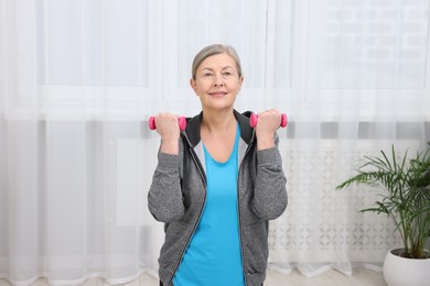 Photo of Smiling elderly woman exercising with dumbbells at home