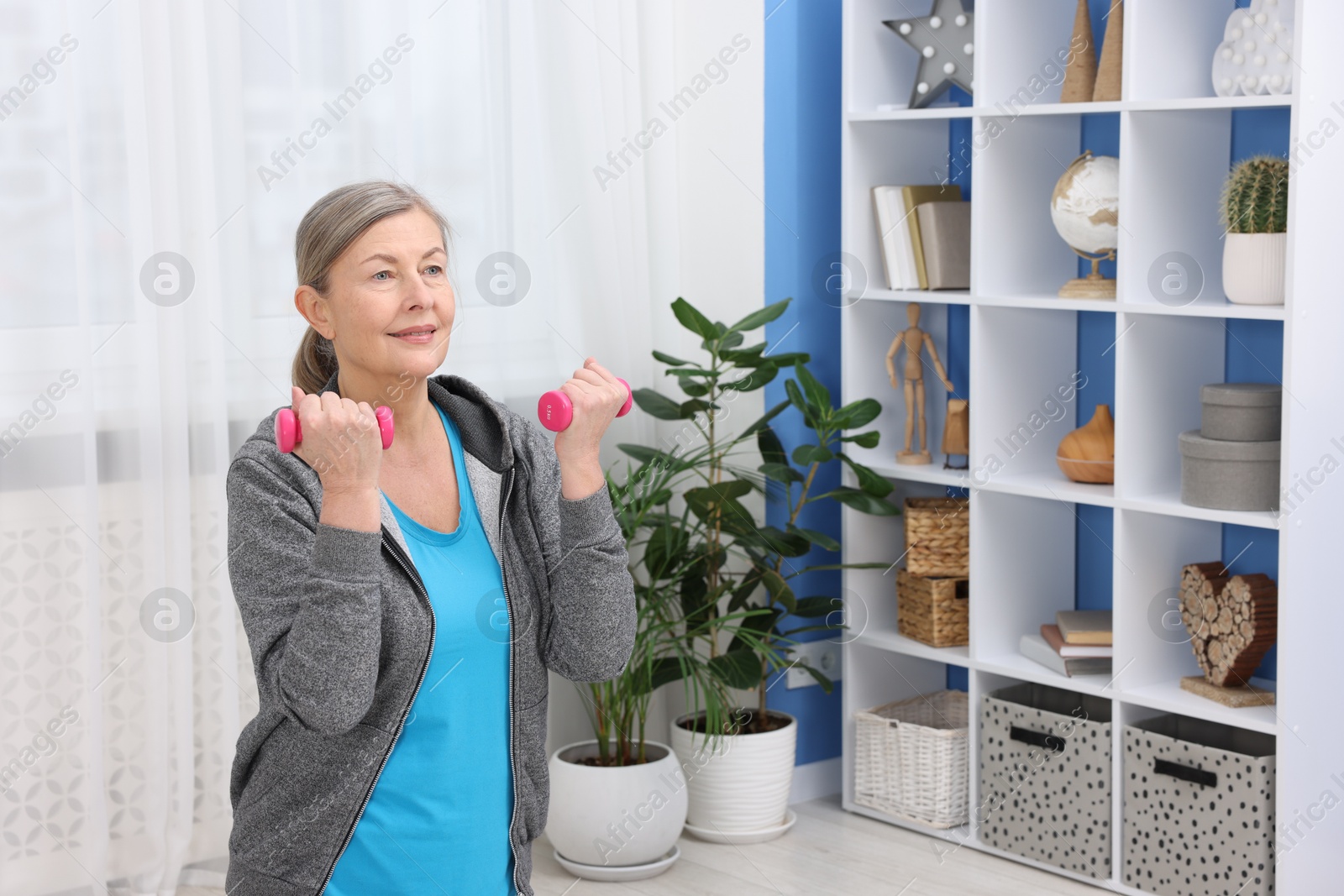 Photo of Smiling elderly woman exercising with dumbbells at home