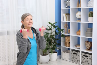 Photo of Smiling elderly woman exercising with dumbbells at home