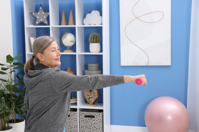 Photo of Smiling elderly woman exercising with dumbbells at home