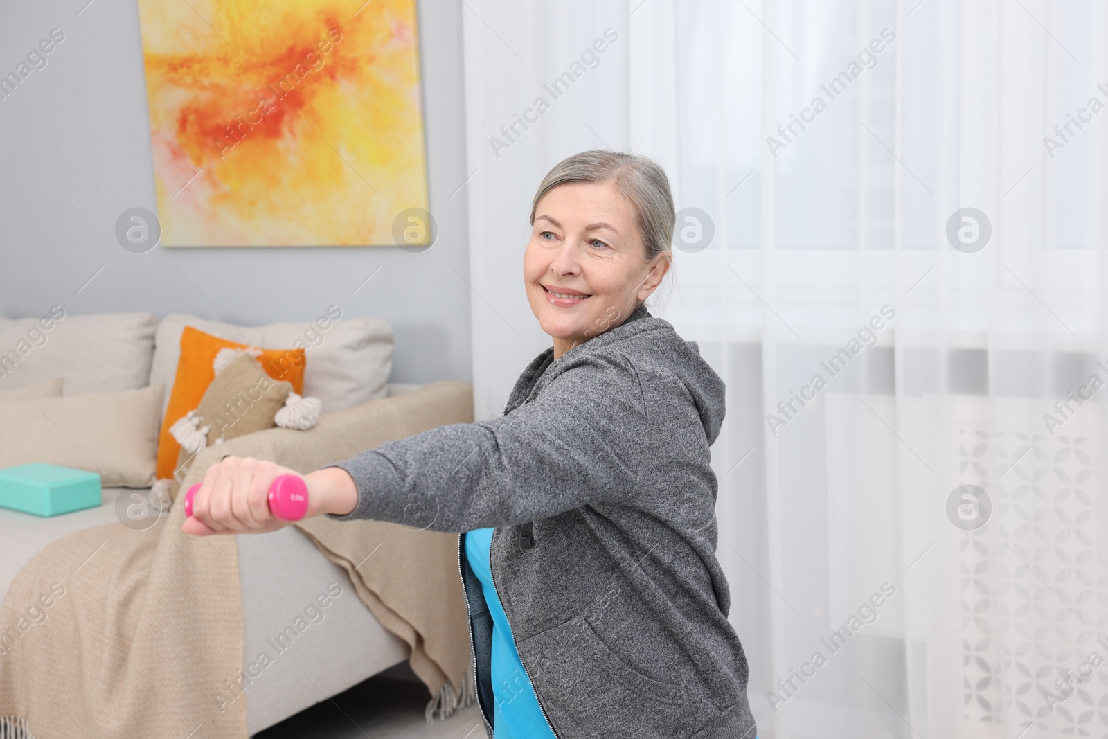 Photo of Smiling elderly woman exercising with dumbbells at home