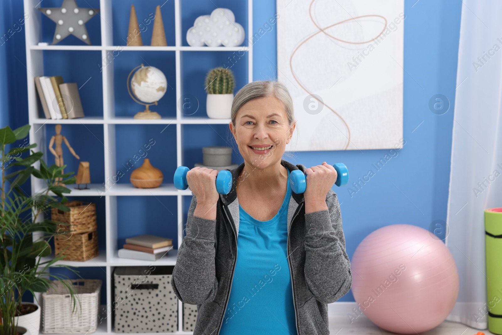 Photo of Smiling elderly woman exercising with dumbbells at home