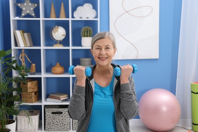 Photo of Smiling elderly woman exercising with dumbbells at home