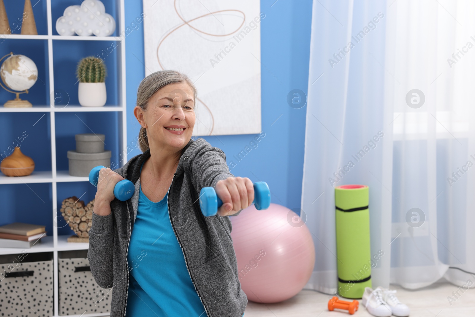 Photo of Smiling elderly woman exercising with dumbbells at home