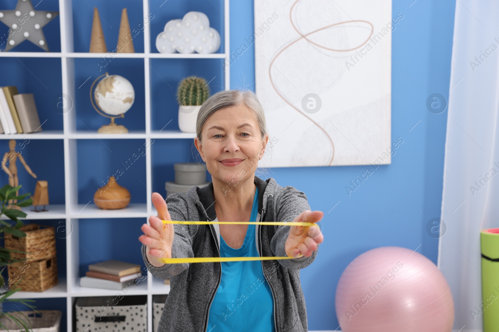 Photo of Elderly woman exercising with fitness elastic band at home