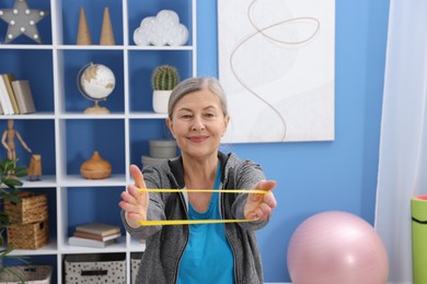 Photo of Elderly woman exercising with fitness elastic band at home