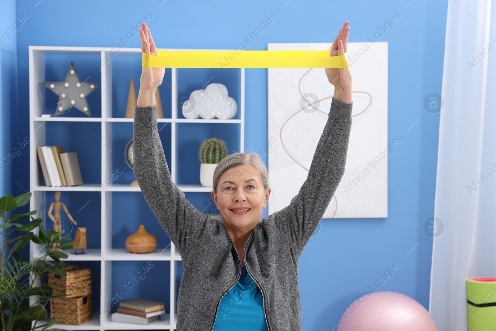 Photo of Smiling elderly woman exercising with fitness elastic band at home