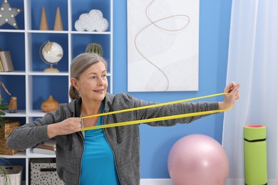 Photo of Smiling elderly woman exercising with fitness elastic band at home