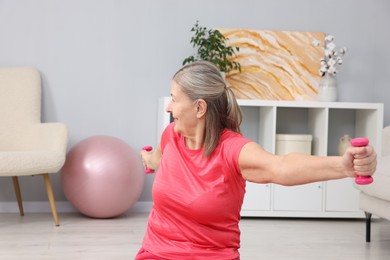 Photo of Elderly woman exercising with dumbbells at home