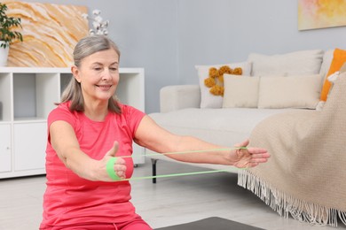 Photo of Smiling elderly woman exercising with fitness elastic band at home