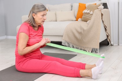 Photo of Elderly woman exercising with fitness elastic band at home