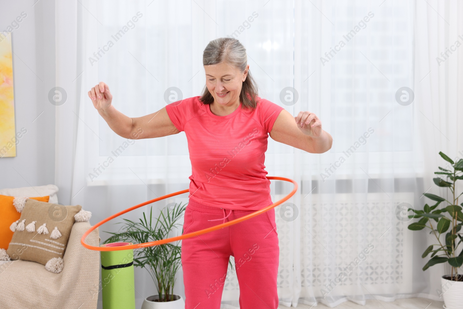 Photo of Smiling elderly woman exercising with hula hoop at home