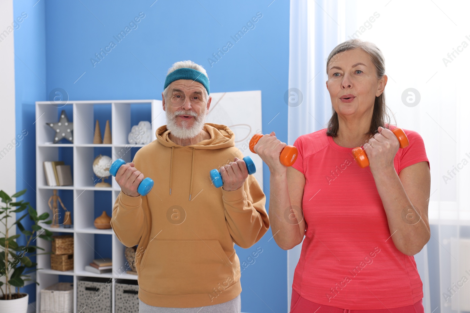 Photo of Elderly couple exercising with dumbbells at home