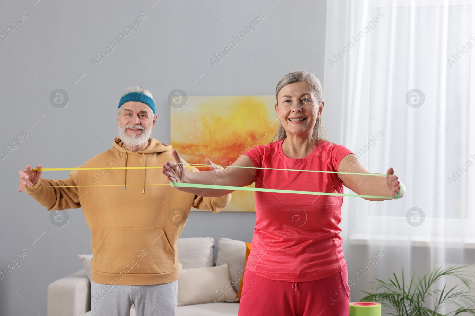 Photo of Smiling elderly couple exercising with fitness elastic bands at home