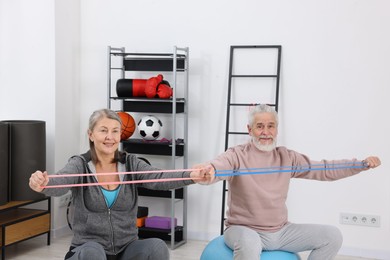 Photo of Smiling elderly couple exercising with elastic bands and fitness balls at home