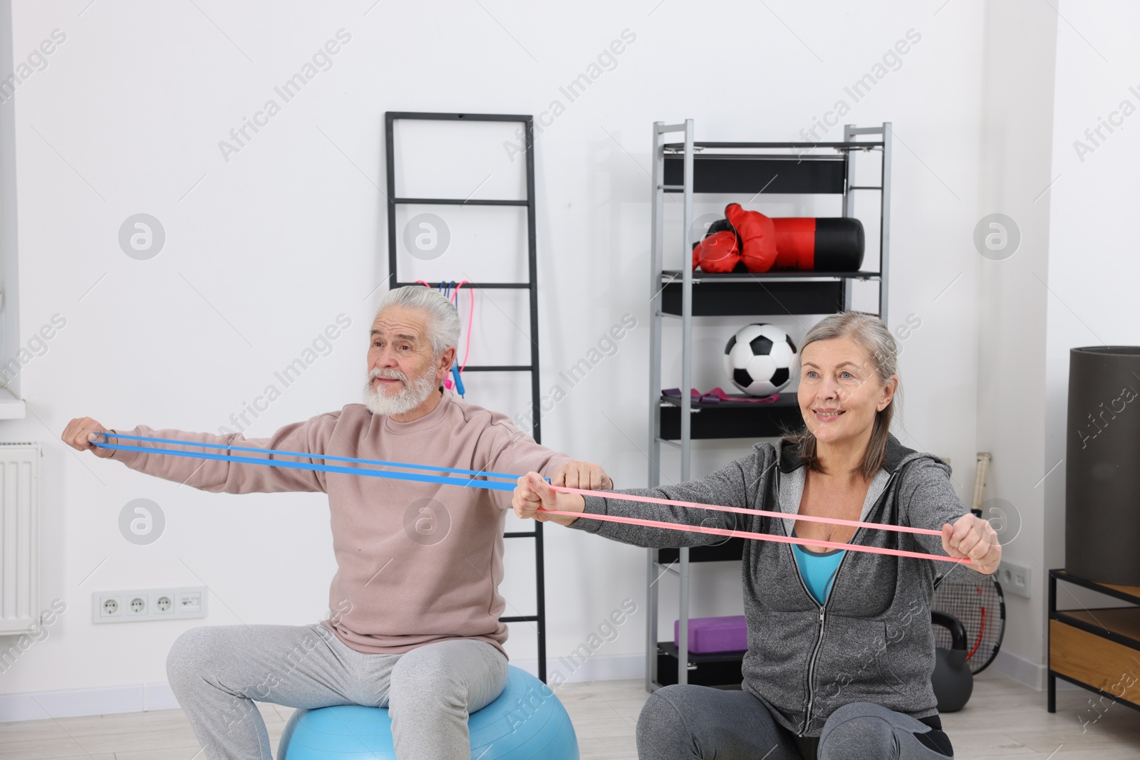 Photo of Smiling elderly couple exercising with elastic bands and fitness balls at home