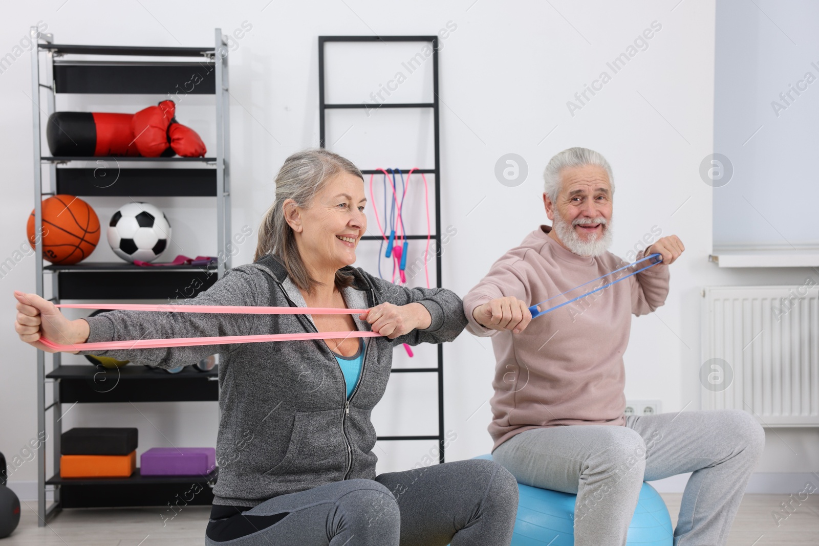 Photo of Smiling elderly couple exercising with elastic bands and fitness balls at home